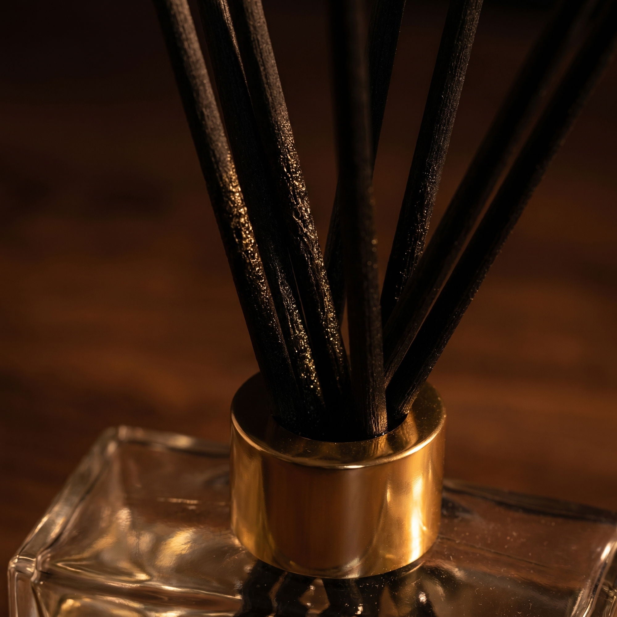 Diffuser with black sticks in a clear container with a gold cap on a dark background