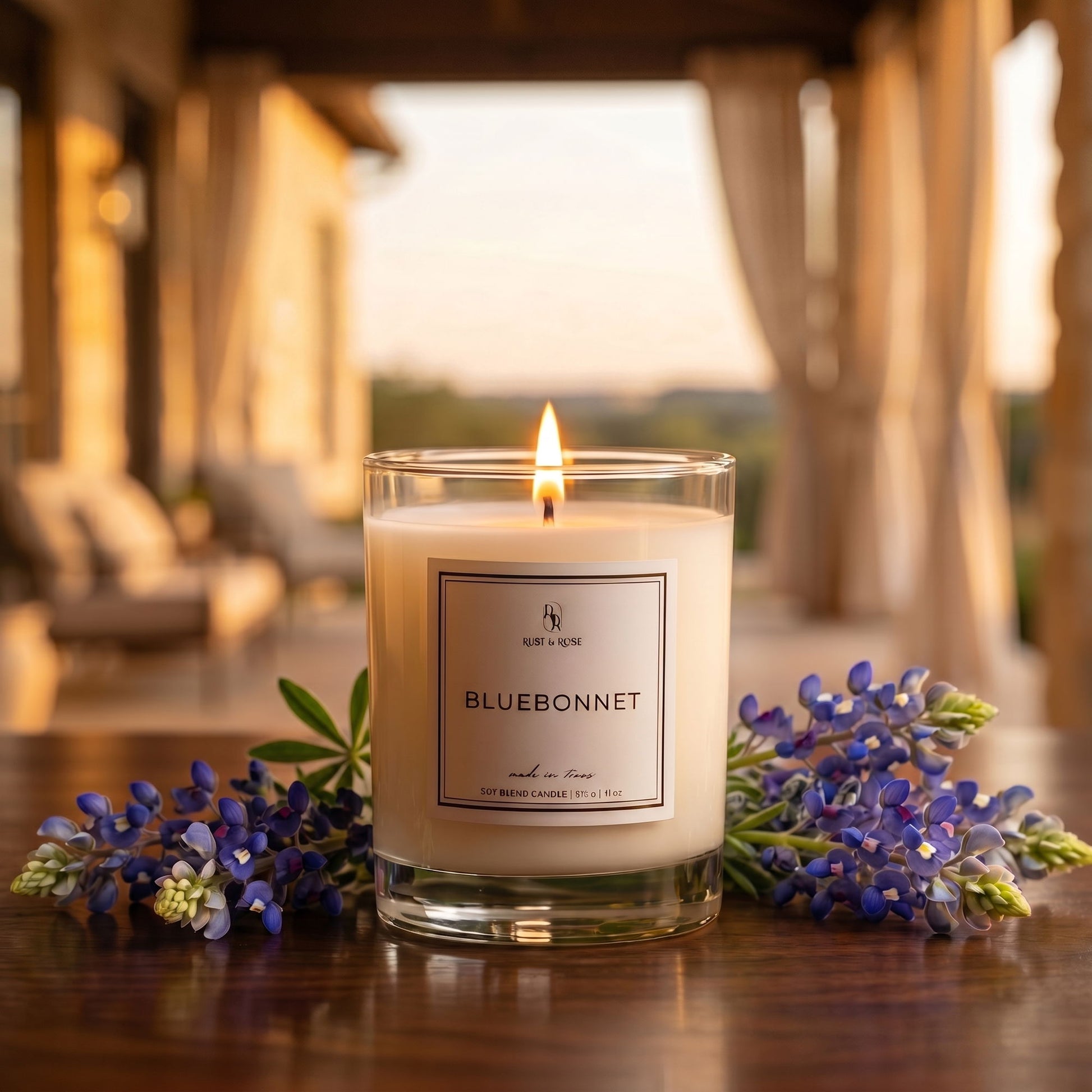 Candle labeled 'Bluebonnet' with flowers on a wooden surface outdoors.