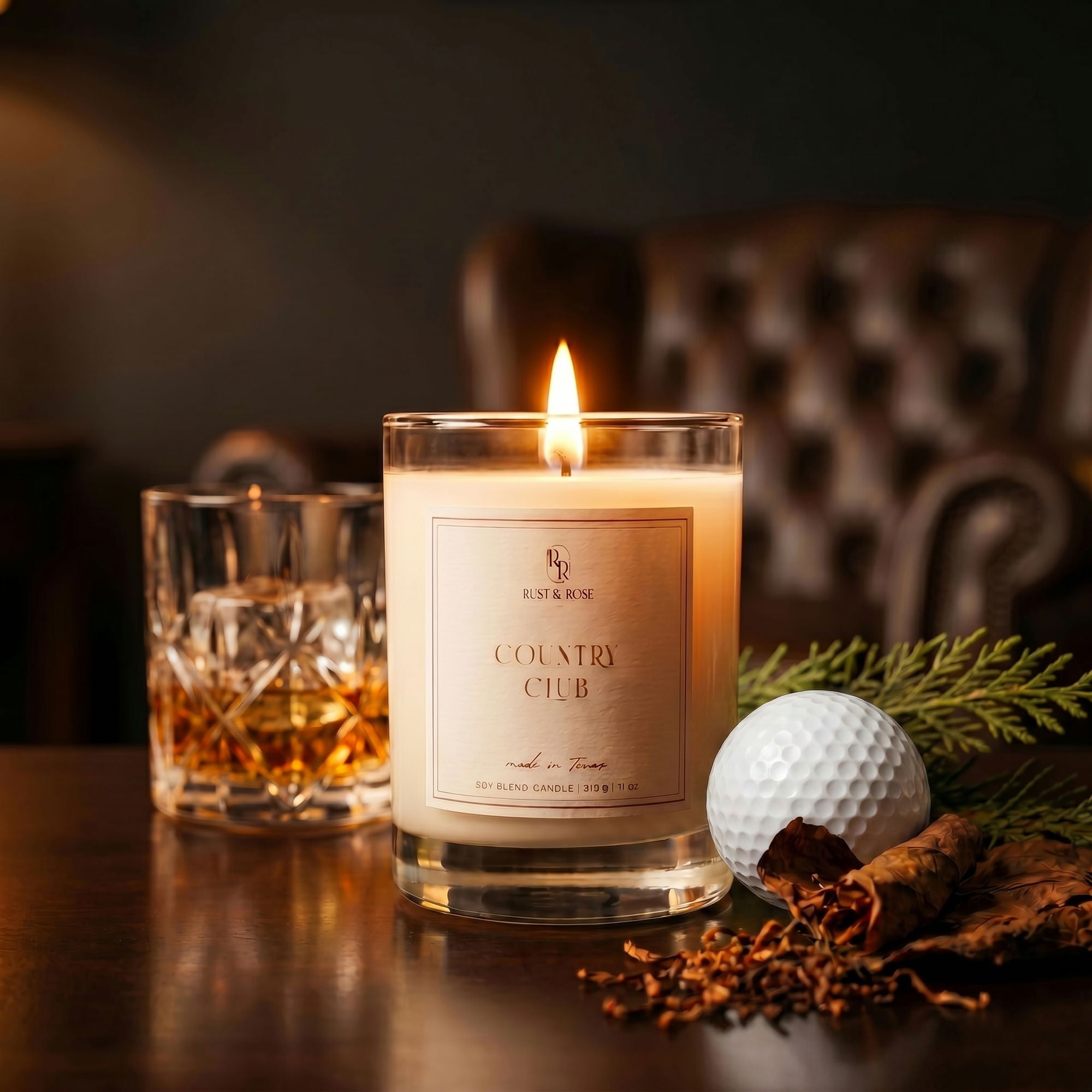 Candle labeled 'Country Club' with a glass of whiskey and a golf ball on a table.