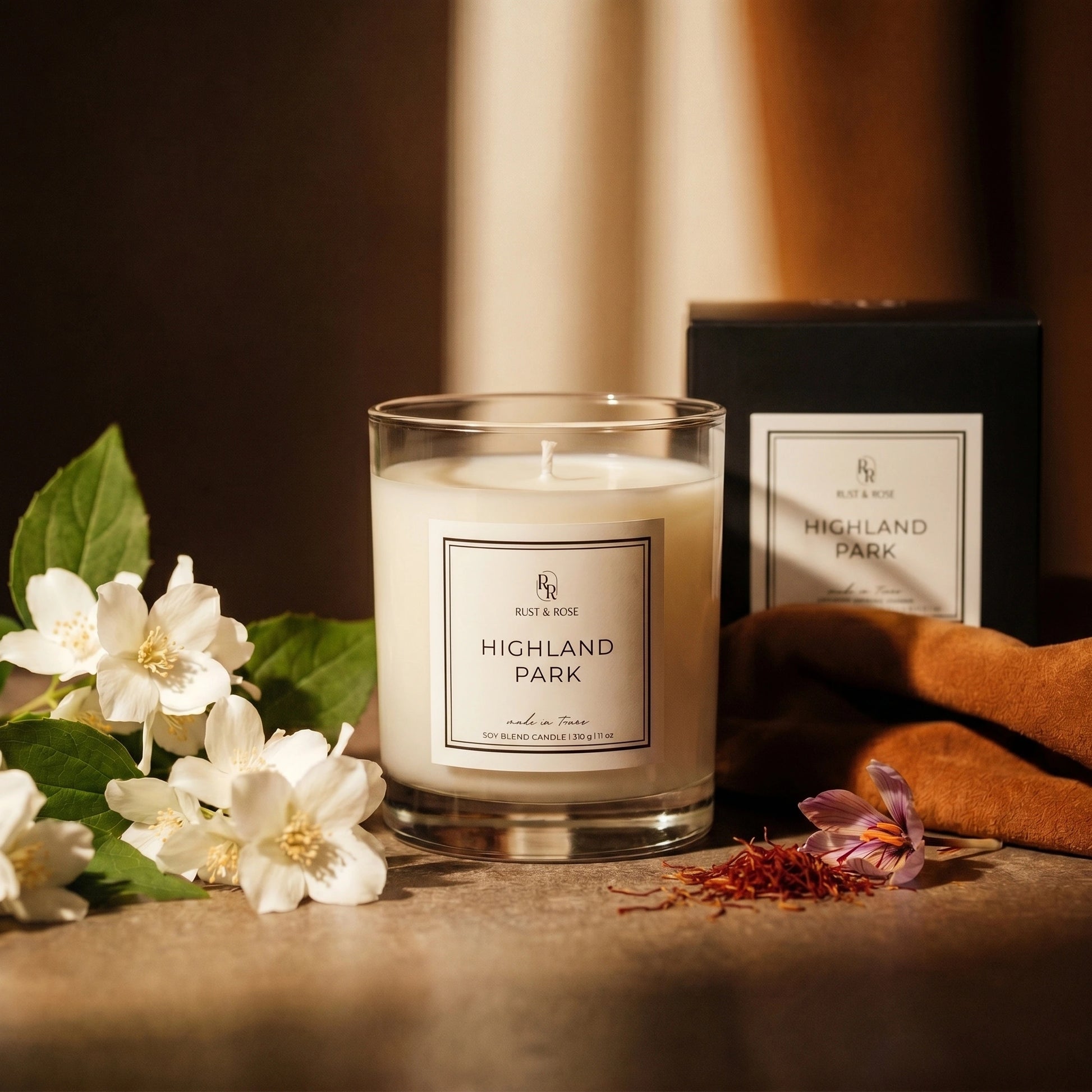 Candle labeled 'Highland Park' with flowers and a box in the background