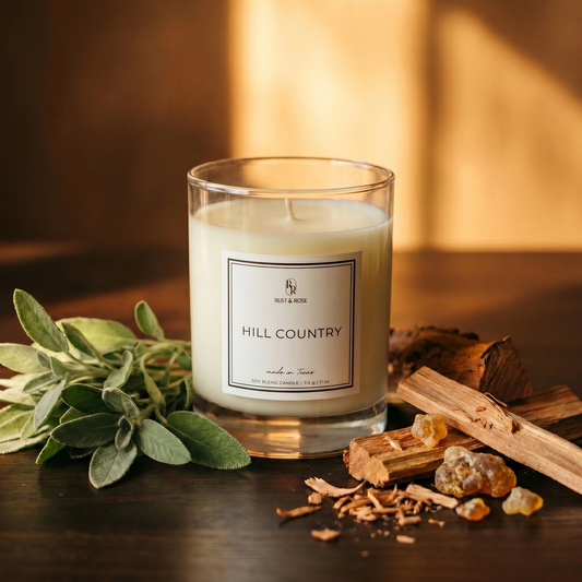 Candle labeled 'Hill Country' with herbs and wood on a wooden surface