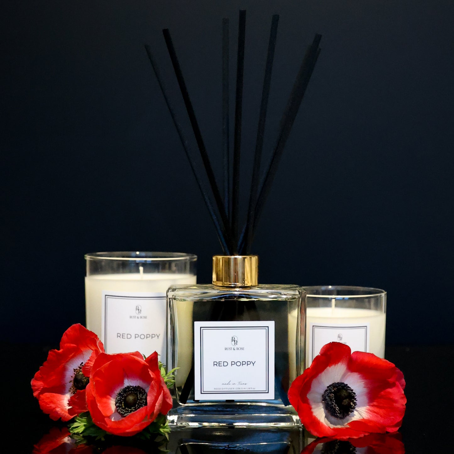 Two candles and a diffuser with red poppy flowers on a black background