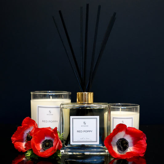 Two candles and a diffuser with red poppy flowers on a black background