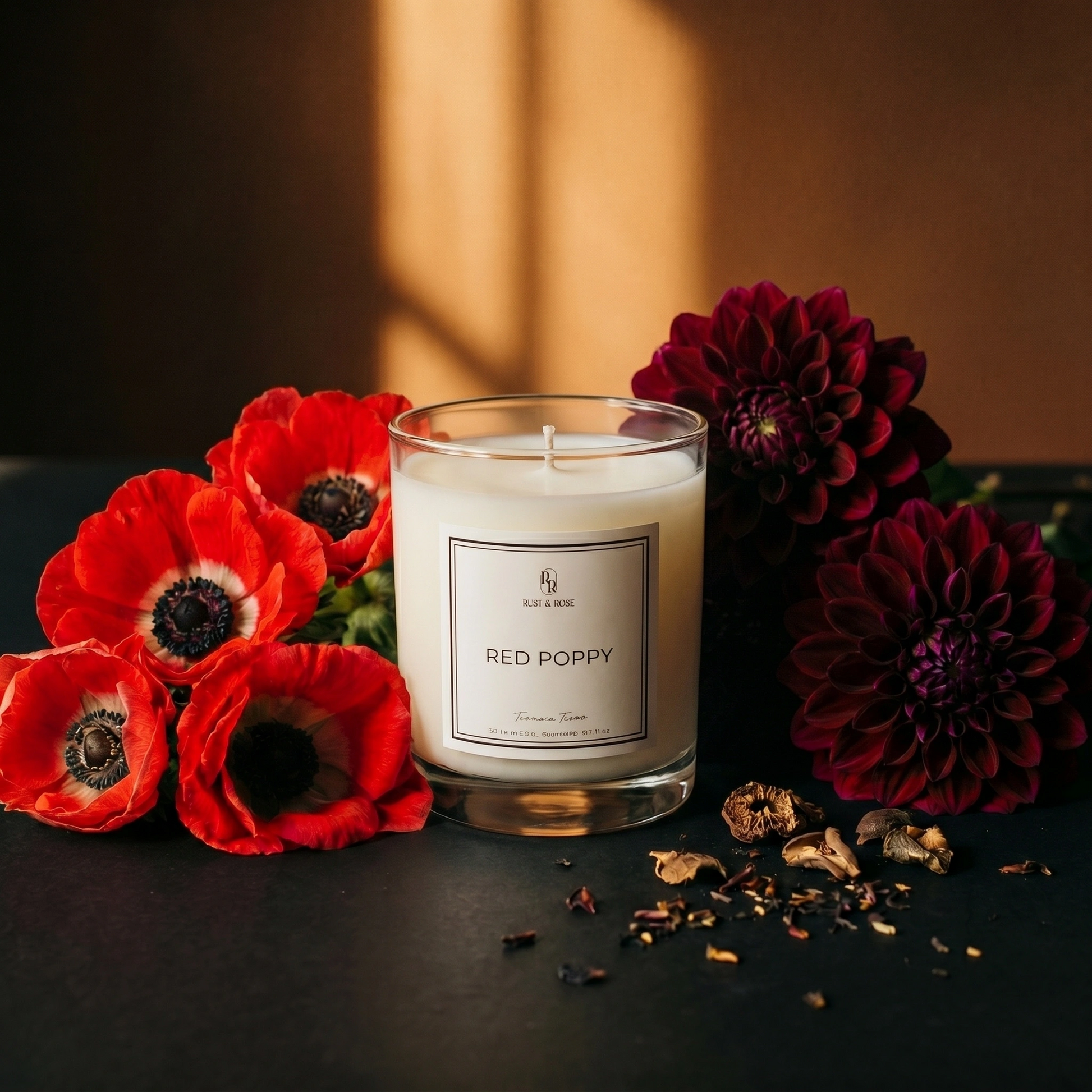 Candle labeled 'Red Poppy' surrounded by red and purple flowers on a dark surface.
