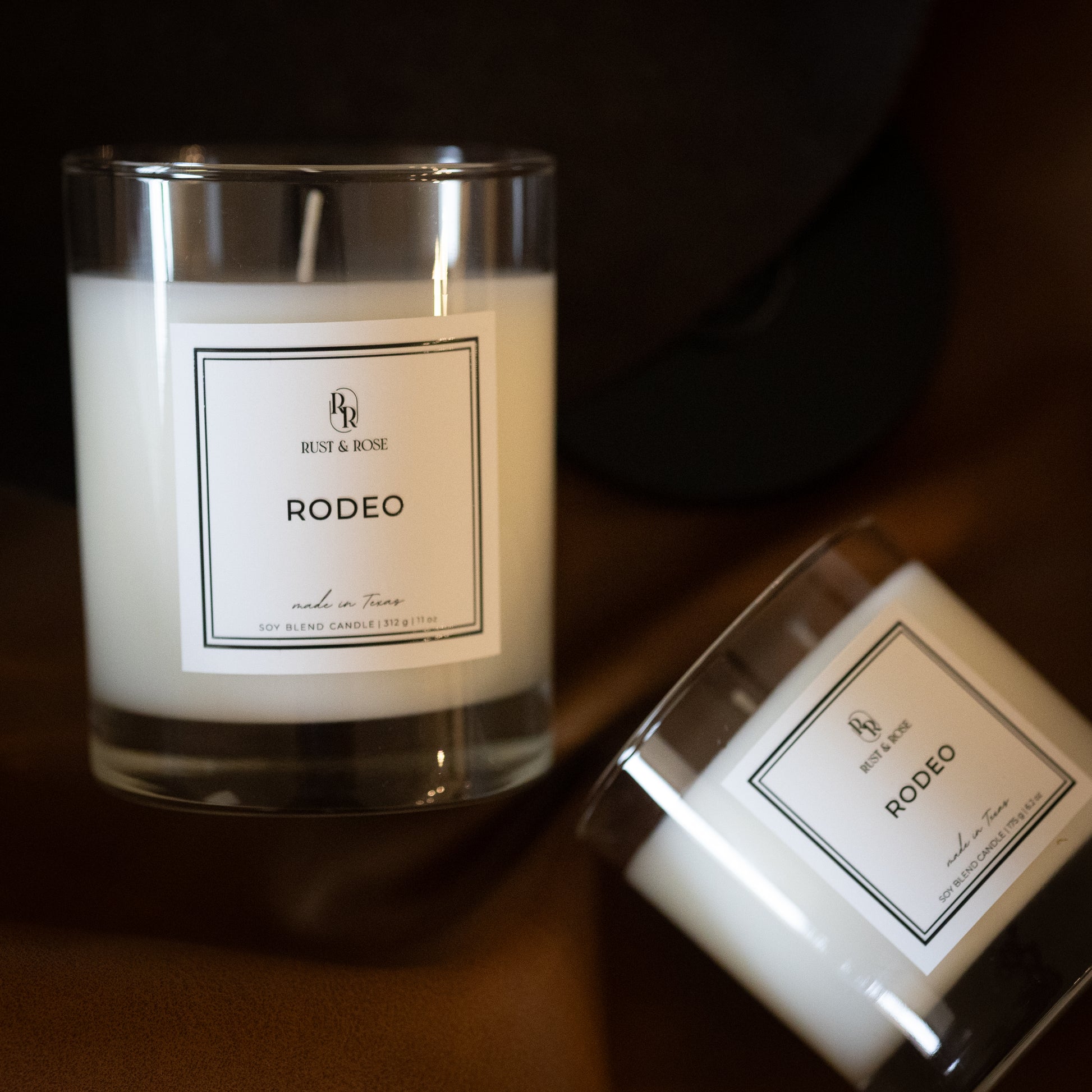 Two candles labeled 'Rodeo' by 'Rose & Rose' on a dark surface.